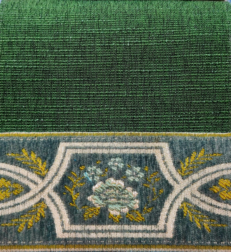 May include: Close-up of a green fabric with a decorative border. The border features a floral design with white and gold accents on a blue background.