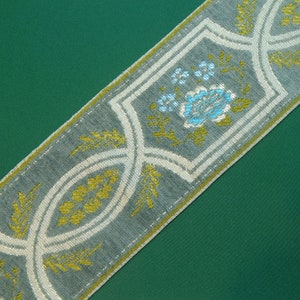 May include: A gray and white fabric trim with a repeating pattern of stylized flowers and leaves in shades of blue, green, and gold.