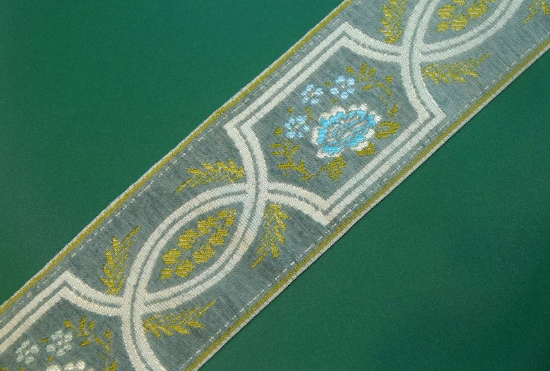 May include: A gray and white fabric trim with a repeating pattern of stylized flowers and leaves in shades of blue, green, and gold.