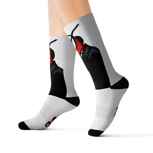 May include: A pair of white socks with a black and red graphic design of a person wearing a hat and a cape. The socks are shown on a model's legs.