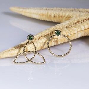May include: A pair of gold earrings with green gemstones. One earring is a circle and the other is a trinity knot design.