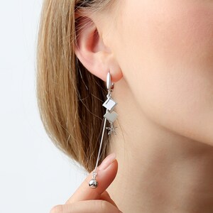 May include: Silver dangle earrings with a square charm, a star charm, and a small ball at the end.