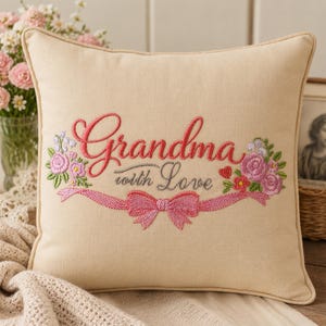 Può includere: Cuscino quadrato beige con ricamo "Grandma with Love" in corsivo rosa. Il testo è circondato da ricami floreali rosa, viola e verdi. Un nastro rosa con un fiocco è sotto il testo.