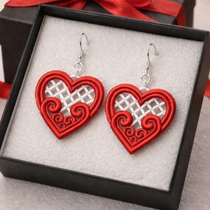 Pode incluir: Brincos em forma de coração com contorno bordado vermelho e design de treliça branca. Os brincos apresentam um padrão de redemoinho decorativo e ganchos prateados. Apresentados numa caixa de presente preta.