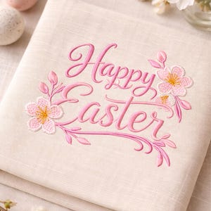 Può includere: Un tovagliolo pasquale in lino beige ricamato con le parole "Happy Easter" in rosa. Accenti floreali e di foglie rosa circondano il testo. Due uova di Pasqua decorative sono visibili sullo sfondo.