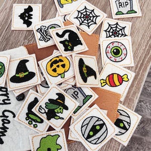 Puede incluir: Una colección de pequeños parches cuadrados con temática de Halloween con diseños bordados. Los parches presentan imágenes de un murciélago, telaraña, gato negro, calabaza, sombrero de bruja, globo ocular, caramelo, lápida, momia y bruja en una escoba. Los parches son blancos con costuras doradas.