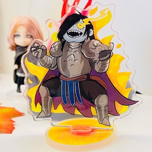 May include: A clear acrylic stand with a yellow and orange flame design. A cartoon character with a black and gray armor, a purple cape, and a yellow eye is standing on the stand.