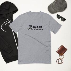 Könnte beinhalten: Ein hellgraues T-Shirt mit schwarzem Text, der "3% human 97% stress" lautet.