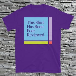 Pode incluir: Camiseta roxa com um gráfico azul, amarelo, rosa e vermelho que diz "This Shirt Has Been Peer Reviewed".