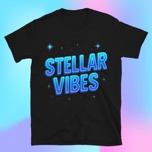 May include: Black t-shirt with the words "STELLAR VIBES" in a gradient blue and white font. The text is surrounded by small star graphics. The shirt is a crew neck style.