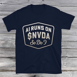 以下が含まれることがあります： 白と金のグラフィックが特徴のネイビーブルーのTシャツ。グラフィックは、白いアウトラインの形の中に、様式化されたフォントで「AI RUNS ON $NVDA So Do I」と書かれています。シャツは柔らかい素材で作られています。