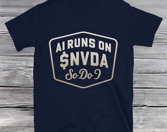 May include: Navy blue t-shirt with a white and gold graphic. The graphic reads "AI RUNS ON $NVDA So Do I" in a stylized font within a white outlined shape. The shirt is made of a soft material.