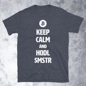 May include: Dark gray t-shirt with the text "KEEP CALM AND HODL $MSTR" in white. A white Bitcoin symbol is above the text. The shirt is a short-sleeved crew neck.