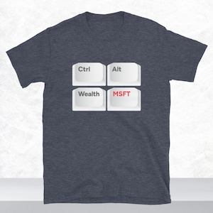 Może przedstawiać: Ciemnoszary melanżowy t-shirt z krótkim rękawem z grafiką przedstawiającą cztery białe klawisze klawiatury komputerowej ułożone w kwadrat. Klawisze mają nadrukowane napisy Ctrl, Alt, Wealth oraz MSFT, przy czym litery MSFT są w kolorze czerwonym.