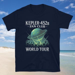 May include: Navy blue t-shirt with a graphic featuring a planet with rings, a crowd silhouette, and the text "KEPLER-452B - FAN CLUB - WORLD TOUR" in white. The design is centered on the shirt.