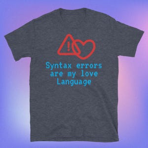 May include: Dark heather grey t-shirt with a blue and red graphic of an exclamation point inside a triangle and a heart. The text "Syntax errors are my love language" is printed in blue.