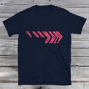 May include: Navy blue t-shirt with the text "FORWARD ONLY" in a pink, layered, slanted design. The shirt is made of a soft material and has short sleeves and a crew neck.