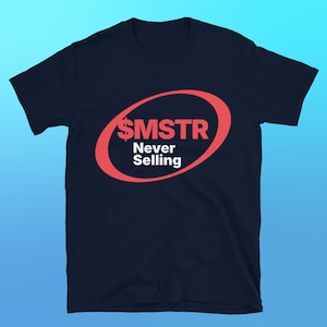 May include: A navy blue t-shirt featuring a red oval design. The design includes the text "$SMSTR" above "Never Selling" in white. The t-shirt is made of a soft material.