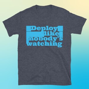 Może przedstawiać: Ciemnoszara koszulka z jasnoniebieskim napisem "Deploy like nobody's watching". Tekst jest ułożony w stos. Koszulka ma krótkie rękawy i okrągły dekolt.
