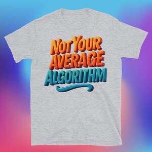 Puede incluir: Camiseta gris claro con el texto "Not Your Average Algorithm" en letras 3D naranjas y azules. La camiseta tiene mangas cortas y cuello redondo. El texto está resaltado con un acento azul.