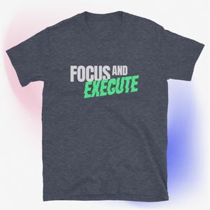May include: Dark gray t-shirt with the words "FOCUS AND EXECUTE" printed on the front. The word "FOCUS" is in white, and "EXECUTE" is in green. The shirt is made of a soft material.