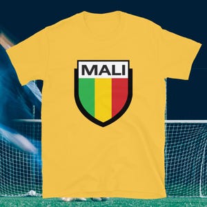 May include: A yellow t-shirt with a shield design. The shield has the word "MALI" in white at the top and vertical stripes of green, yellow, and red. The shirt is short-sleeved.