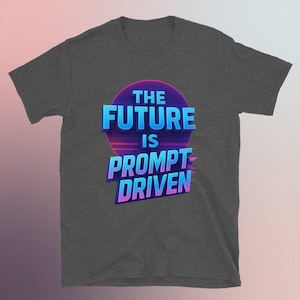 May include: Dark grey t-shirt featuring the text "THE FUTURE IS PROMPT DRIVEN" in a retro font. The text is in blue and purple, set against a purple and pink circular background.