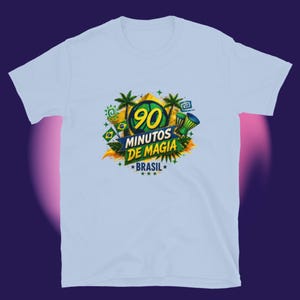 Puede incluir: Camiseta azul claro con un diseño gráfico colorido. El diseño incluye el texto "90 MINUTOS DE MAGIA BRASIL" en amarillo y verde, junto con elementos de la bandera brasileña, palmeras y estrellas. La camiseta está hecha de un material suave.