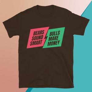 May include: A brown t-shirt with the text "BEARS SOUND SMART" in pink and "BULLS MAKE MONEY" in green. The text is arranged in a diagonal layout with a lightning bolt graphic.
