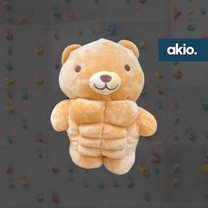 Peut inclure: Un ours en peluche avec un visage brun et un corps brun clair. L'ours porte un costume musculaire avec un six-pack bien défini.