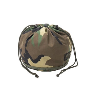 May include: A camouflage drawstring bag with a green drawstring closure. The bag features a pattern of brown, green, and tan shapes. A small rectangular patch with the letters "MIS" is on the lower right side of the bag.