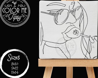 May include: Black and white line art drawing of a woman wearing sunglasses and holding a lollipop. The drawing is on a white canvas and is mounted on a wooden easel. The text "COLOR ME TIPSY" is visible in the lower right corner of the canvas.