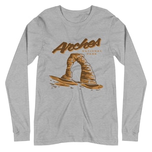 May include: A gray long-sleeve t-shirt with a brown illustration of Delicate Arch in Arches National Park. The text "Arches National Park" is printed in brown above the arch.