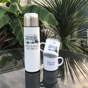 May include: White insulated travel mug with a black and white illustration of a camper van and the text "Home is where we park it!"  Two white enamel mugs with black and white camper van illustrations. The top mug has the name "Sue" on it. The bottom mug has the text "Time for a brew!"