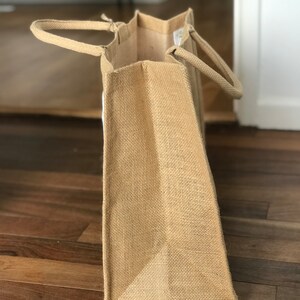 May include: A large, brown burlap tote bag with two handles. The bag is made of natural, woven fabric and has a slightly textured surface.