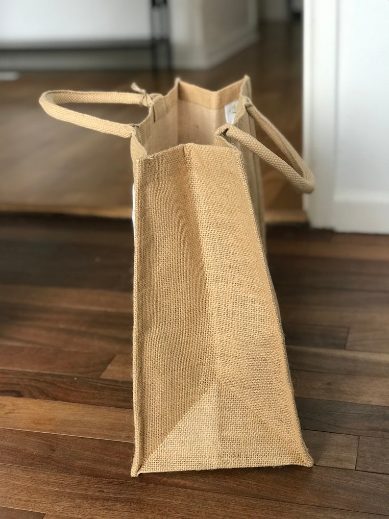 May include: A large, brown burlap tote bag with two handles. The bag is made of natural, woven fabric and has a slightly textured surface.