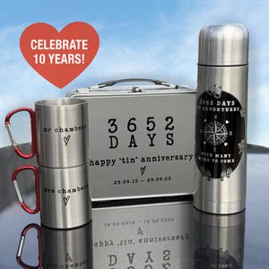 May include: A set of anniversary gifts in stainless steel. The image shows two mugs with red handles, a lunchbox, and a flask. Text includes "Celebrate 10 Years!" and "3652 Days of Adventures" and a compass.