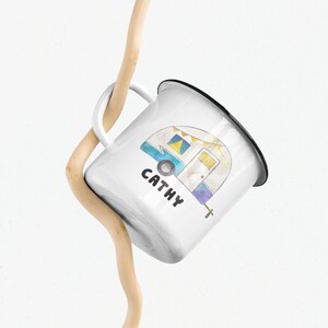 May include: White enamel mug with a black rim and handle. The mug features a watercolor illustration of a camper van with the name "Cathy" printed below it.