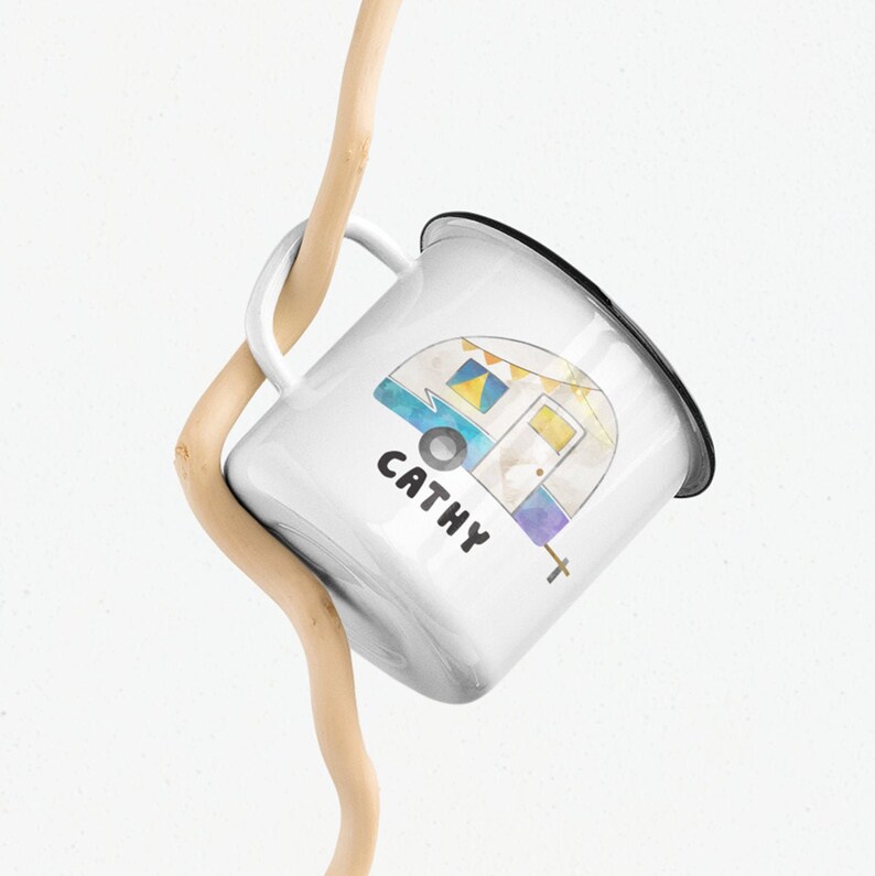 May include: White enamel mug with a black rim and handle. The mug features a watercolor illustration of a camper van with the name "Cathy" printed below it.