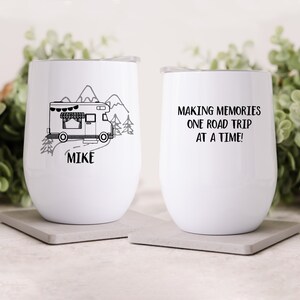 Peut inclure: Deux gobelets à vin en acier inoxydable blanc. Un gobelet présente une illustration en noir et blanc d'un camping-car conduisant dans un paysage de montagne avec le nom "Mike" en dessous. L'autre gobelet porte le texte "Making memories one road trip at a time!"
