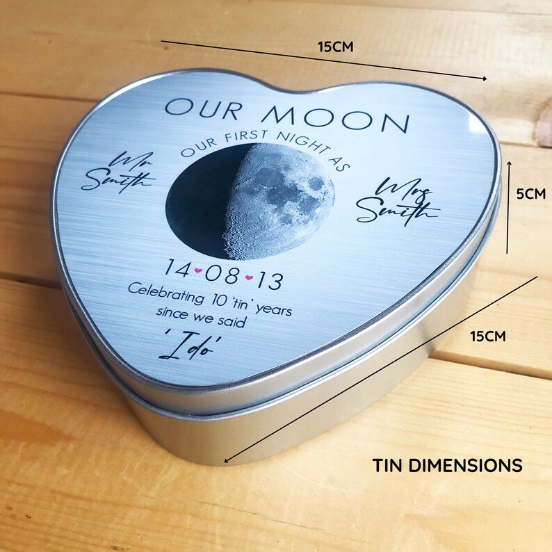 May include: A silver heart-shaped tin with a moon and stars design. The tin is 15 cm wide and 5 cm tall. It says "Our Moon, Our First Night As" with the date "14-08-13" and "Celebrating 10 'tin' years since we said 'I do'."