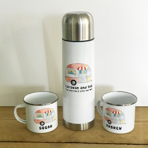 May include: Two white enamel mugs with a cartoon caravan design and the names "Susan" and "Andrew" printed on them. A white stainless steel thermos with a cartoon caravan design and the text "caravan and tea the perfect life for me!" printed on it.