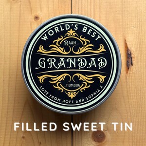 May include: A round, black tin with gold and white text that reads "WORLD'S BEST GRANDAD." The tin has a decorative border and the words "LOVE FROM HOPE AND SOPHIA X." The text "FILLED SWEET TIN" is at the bottom.