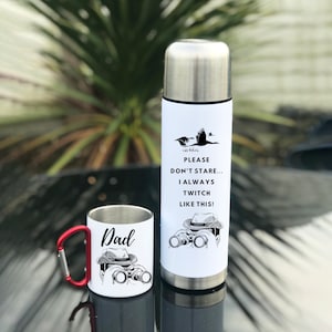 May include: A white insulated travel mug with a black and white illustration of a person wearing a hat and holding binoculars. The text "Please don't stare... I always twitch like this!" is printed on the mug. A white mug with a red handle and the word "Dad" printed on it is also shown. The mug has a black and white illustration of a person wearing a hat and holding binoculars.