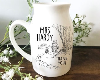 May include: White ceramic pitcher with a handle, featuring a black and white illustration of Winnie the Pooh and Piglet walking on a path. The text "MRS HARDY THANK YOU!" is printed on the pitcher.
