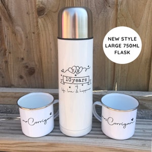May include: White insulated flask with a black design that says "10 years of life, love & happiness" with two hearts and the initials "M & R". The flask is accompanied by two white enamel mugs with black lettering that says "Mr. Corrigan" and "Mrs. Corrigan".