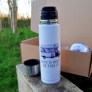May include: White insulated travel mug with a black lid and a graphic of a camper van with the text "Home is where we park it!" printed on the side.