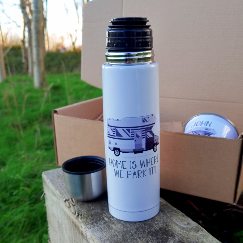 May include: White insulated travel mug with a black lid and a graphic of a camper van with the text "Home is where we park it!" printed on the side.