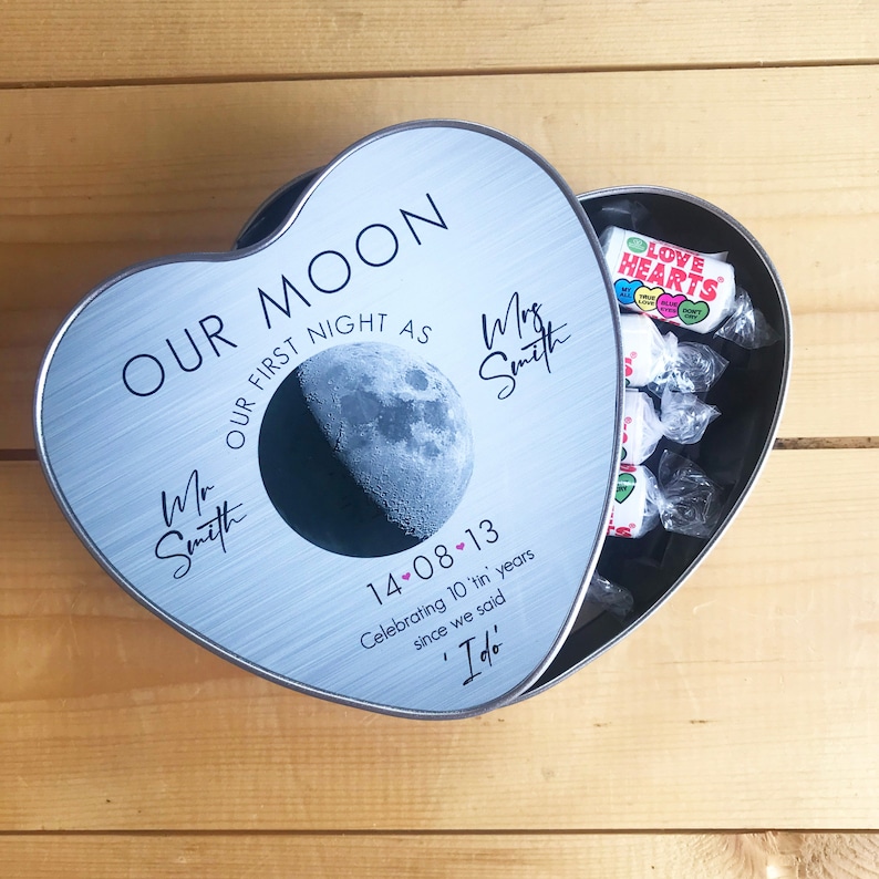 May include: A silver heart-shaped tin with the text "Our Moon Our First Night As" and the date "14-08-13". The tin is open and contains a variety of wrapped candies.