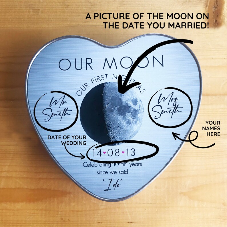 May include: A heart-shaped tin with a picture of the moon on the date of your wedding. The tin is silver with a blue and white moon image. The text "OUR MOON" is printed in black at the top of the tin. The text "OUR FIRST NIGHT AS" is printed in black below the moon image. The text "DATE OF YOUR WEDDING" is printed in black below the text "OUR FIRST NIGHT AS". The date "14-08-13" is printed in black below the text "DATE OF YOUR WEDDING". The text "Celebrating 10+ years since we said 'I do'" is printed in black below the date. The text "YOUR NAMES HERE" is printed in black in the bottom right corner of the tin.
